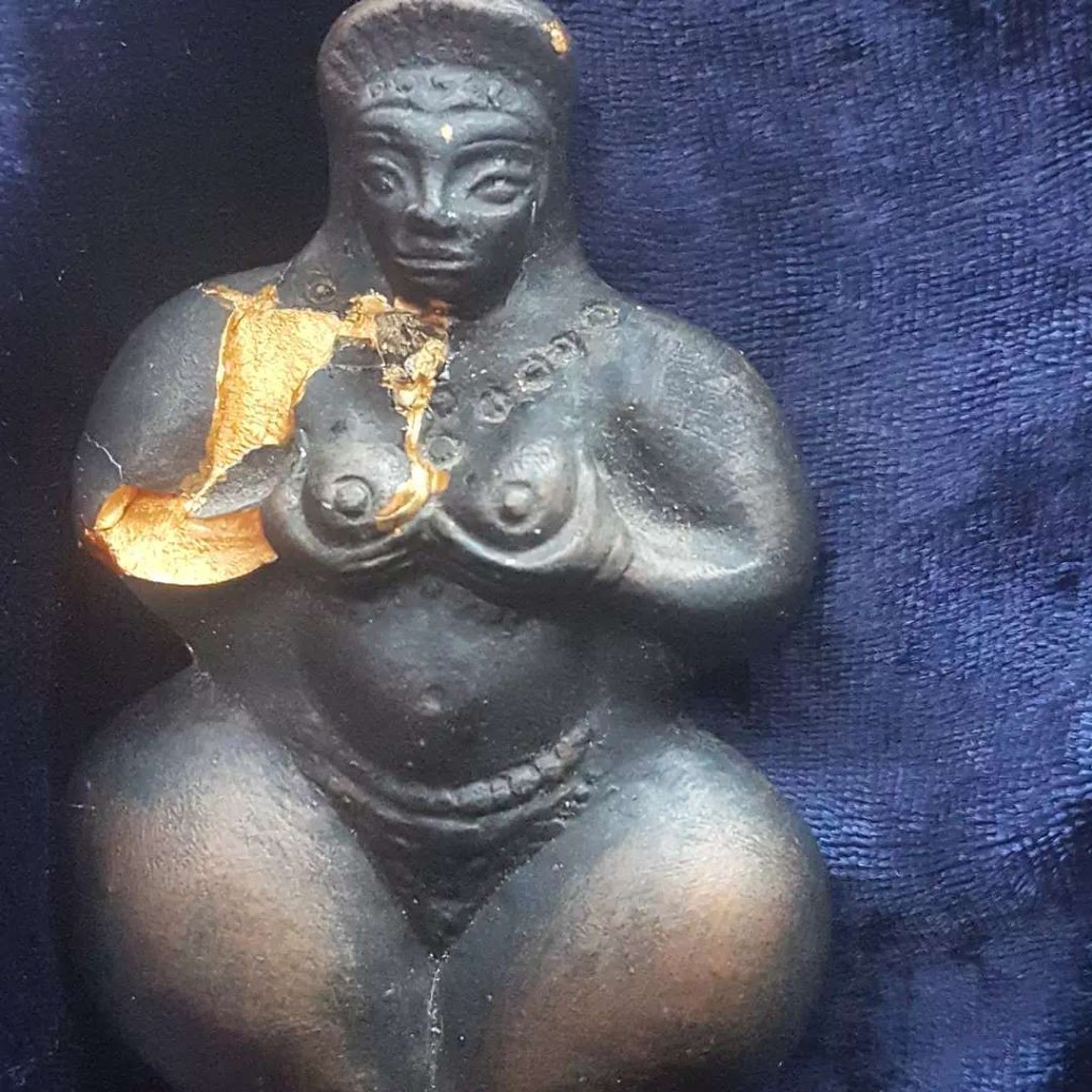Dark goddess figurine with a gold mend on the shoulder, against deep blue velvet